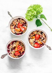 Plum, nectarines, black currant, strawberry crumble in portion forms on a light background, top view