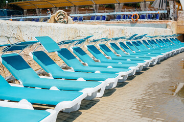 A lot of new beautiful blue sun loungers are standing near the pool in the hotel on a sunny day. Happy vacation vacation. Summer holidays and tourism.