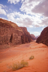 There is a canyon between red relief mountains, there are beautiful clouds in a beautiful sky, the Wadi Rum desert, the nature of Jordan