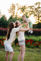 A young homosexual family of mothers hugs and plays in the park with their young son during sunset. Modern happy lesbian family.