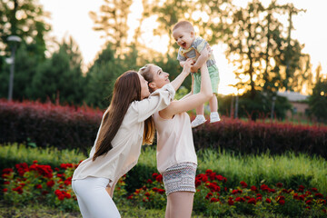 Fototapeta premium A young homosexual family of mothers hugs and plays in the park with their young son during sunset. Modern happy lesbian family.
