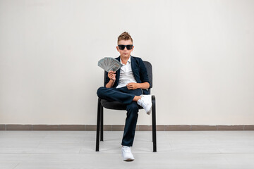 A rich boy on a light background holds a bundle of dollars in his hands. Financial education, young...