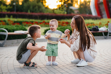 A young beautiful mother with two little boys is playing in the park during sunset. Happy family walk with children in the park.