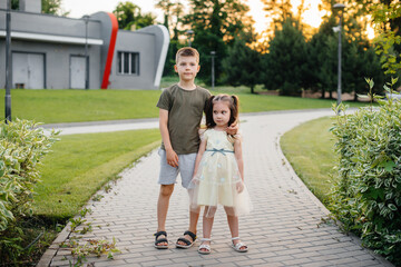 Brother and sister run, play and have fun in the park on a summer day during sunset. Happy childhood.