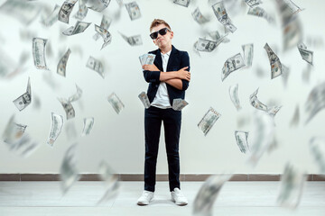 A cute, rich boy with glasses holds dollars and knows how to make money against the background of falling banknotes. Money rain, Financial education, young millionaire, investments, loans, winnings.