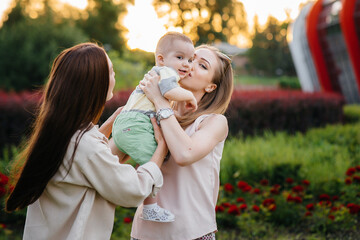 A young homosexual family of mothers hugs and plays in the park with their young son during sunset. Modern happy lesbian family.