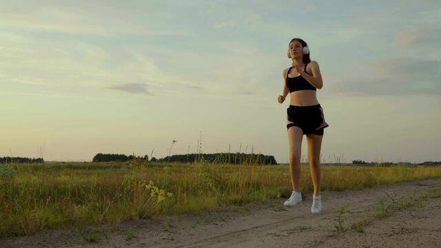 Healthy jogging and outdoor exercise concept. Free young woman runs in summer in park at dawn listens to music with headphones. Training jogging. Listen to music without the Internet and play sports