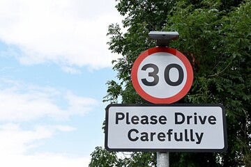 Fototapeta UK road sign 30mph Please Drive Carefully... Blue cloudy sky. obraz