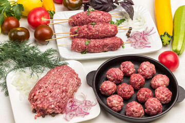 Raw minced meat on plate. Raw meat balls in frying pan. Raw kebab on wooden skewer. Vegetables and greens on table