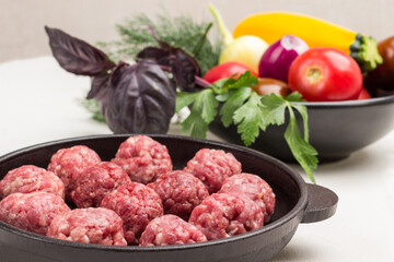 Raw meat balls in frying pan. Vegetables and greens in plate.