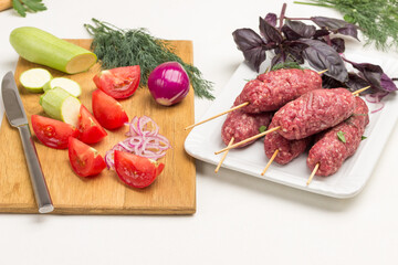 Sliced tomatoes and zucchini on cutting board. Raw minced meat on wooden skewers