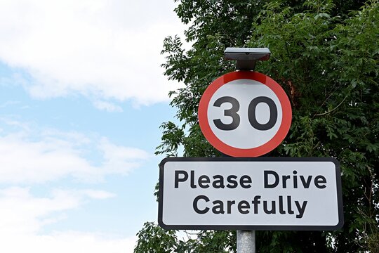 UK road sign 30mph Please Drive Carefully... Blue cloudy sky.