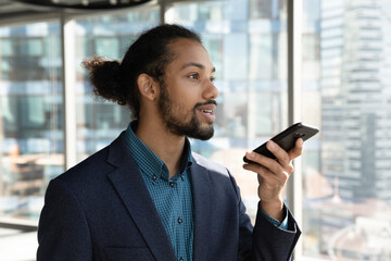 Concentrated young male african american multiracial ceo executive manager entrepreneur recording audio message on smartphone, dictating business ideas, setting reminder or using voice assistant.
