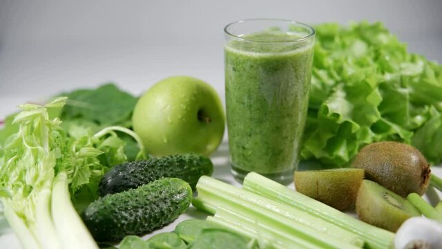 A glass of fresh, healthy celery, green apple, cucumber and kiwi smoothie. Vegetables and fruits lie around the glass. Diet breakfast. Detox. Close-up, the camera rotates around, white background.