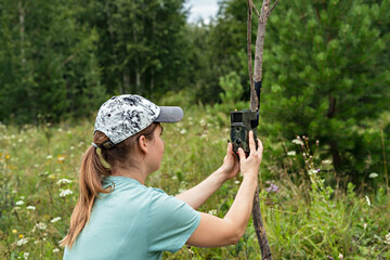 Young woman scientist biologist zoologist sets camera trap for observing wild animals in summer taiga forest to collect scientific data Environmental protection, monitoring of rare and endangered anim