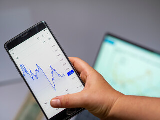 Businessperson checking a stock market graph on a cellphone. Finance and economy going bad, losing money. stock statistics seen on a mobile phone screen for analysis. Project financial stats sales
