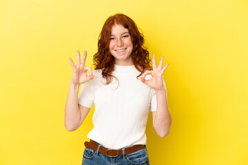 Teenager reddish woman isolated on yellow background showing ok sign with two hands