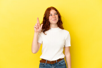 Teenager reddish woman isolated on yellow background with fingers crossing and wishing the best