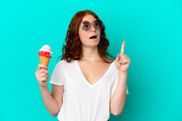 Teenager reddish woman with a cornet ice cream isolated on blue background thinking an idea...