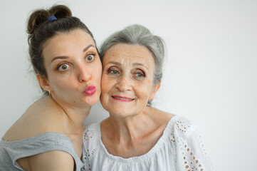 Happy senior mother is hugging her adult daughter, the women are laughing together, sincere family of different age generations having fun on white background, mothers day.