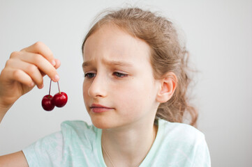 Happy surprised little girl holds cherries in hand. Healthy eating concept, healthy sweets