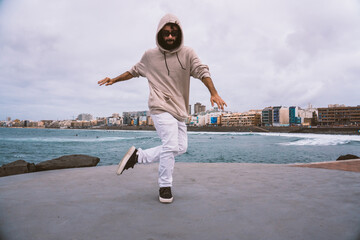 Young caucasian man, wearing casual clothes, dancing urban dances on the beach avenue