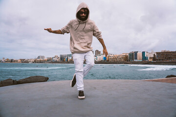 Young caucasian man, wearing casual clothes, dancing urban dances on the beach avenue