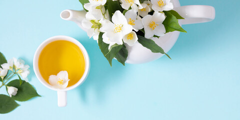 Jasmine tea and jasmine flowers. Teapot with jasmine flowers on blue background. Flat lay, top view, copy space