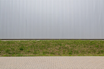 Exterior wall of warehouse made of aluminum sheet and paved sidewalk in outdoor area as background image. 