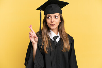 Young university graduate isolated on yellow background with fingers crossing and wishing the best