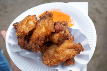Hand hold asian style Fried chicken and spicy sweet and sour sauce on white paper plate.  