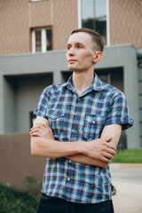 A young man, arms crossed, poses at a photo shoot in a checkered shirt with short sleeves.