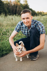 A young man poses for a photo shoot near a pond with a Chihuahua dog.