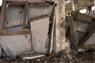 Fototapeta na wymiar A pile of gray concrete slabs of the remains of the building in close-up against the background of the frame of the destroyed building. Background