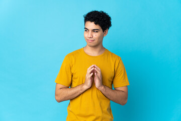 Young Venezuelan man isolated on blue background scheming something