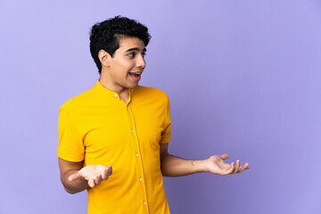 Young Venezuelan man isolated on purple background with surprise expression while looking side