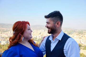 Caucasian plus size red headed woman and her turkish beloved man look to each other. Mixed race couple on a romantic date. Middle eastern man and caucasian woman marriage or engagement
