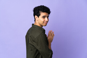 Young Venezuelan man isolated on purple background scheming something
