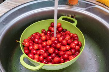 Washing red sweet cherries under the tap in a green bowl, colander close up