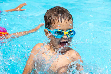 Naklejka premium Little child swims in the pool, plays splashing water