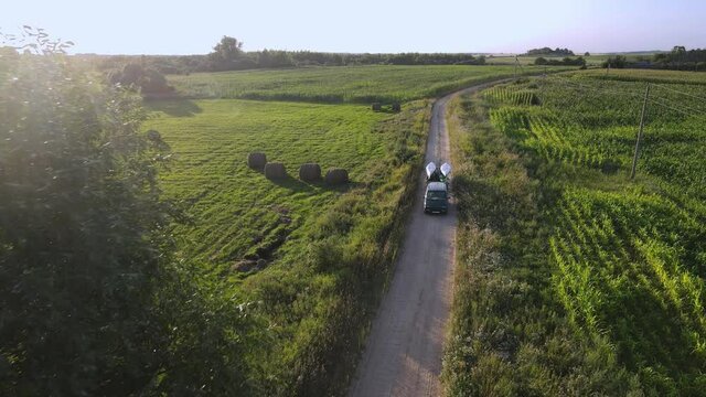 The green car with a trailer carries kayaks and canoes on a rural road. Aerial view. 4K.
