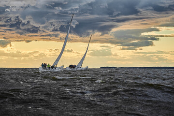 Competition of two sailboats on the horizon in sea at sunset, the amazing storm sky of different...
