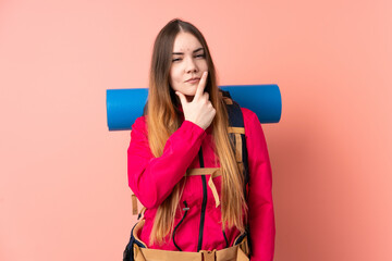 Young mountaineer girl with a big backpack isolated on pink background thinking an idea