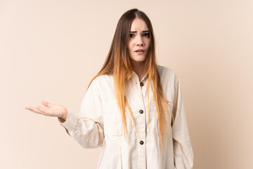 Young caucasian woman isolated on beige background making doubts gesture