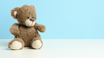 cute brown teddy bear sitting on a white table, blue background