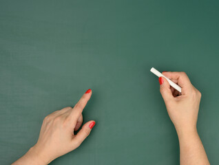 Naklejka premium hand holds a piece of white chalk on the background of an empty green chalk board, presentation concept
