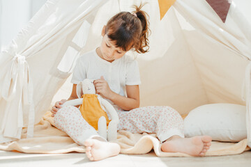 Obraz na płótnie Canvas Six years cute girl playing in teepee with fabric tilda bunny at home