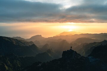 Man stands alone on the peak of rock during sunrise at Pico do Arieiro in Madeira. High quality...