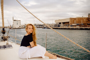 A beautiful long-haired girl sits on the bow of a barred yacht and enjoys life. The blonde is...