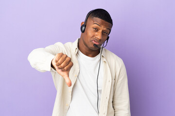 Telemarketer latin man working with a headset isolated on purple background showing thumb down with...